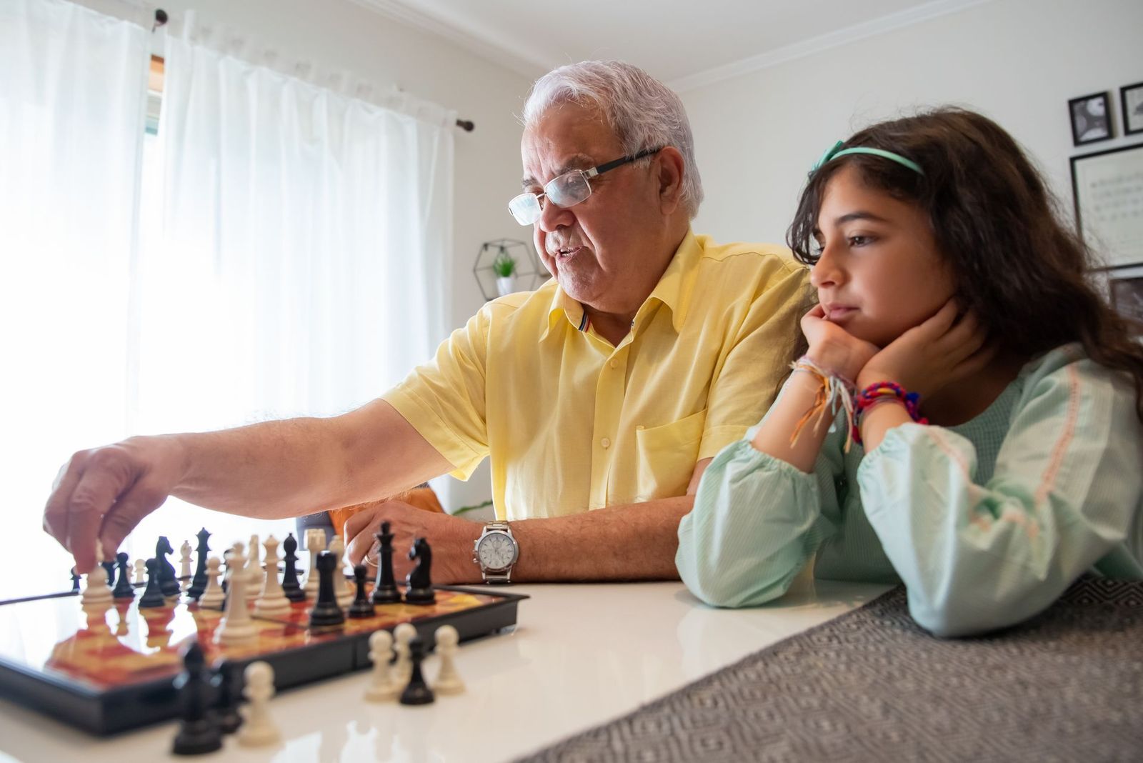 Older man and a girl thinking through a game of chess