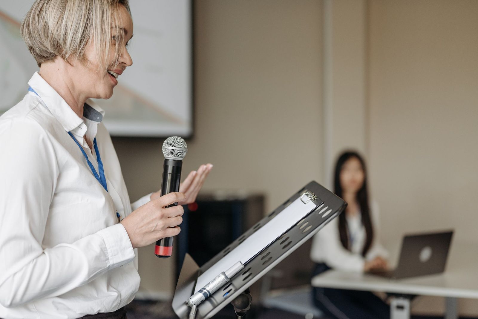 Woman presenting with a microphone and a tablet at a seminar